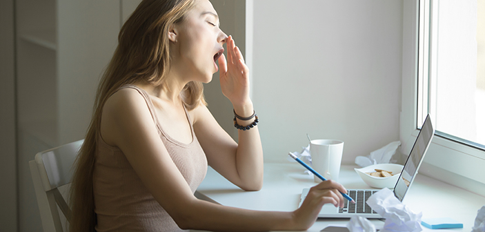 Profile portrait of a young attractive woman in a casual wear yawning at the laptop, , overworked working at laptop, small home office interior, and crumpled paper around. Business concept photo, lifestyle